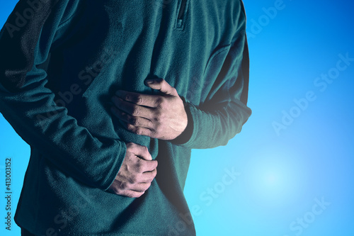 Man holds his belly with both hands against a blue background.