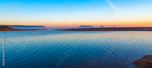 Mouth of the river Ter in the Mediterranean Sea with the Medes Islands and Estartit in the background. Panoramic sunrise landscape with the river flowing calmly. Morning lights with calm atmosphere.