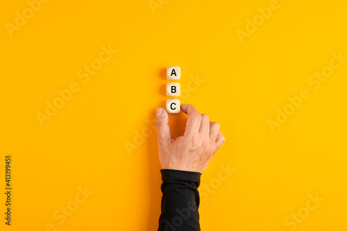 Male hand placing three wooden blocks with the letters of a b and c on yellow background.