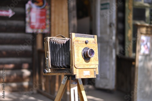 Vintage camera on a tripod on the background of an old wooden hut. A camera from the late 19th or early 20th century. 