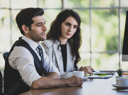 Side view portrait of a thoughtful young adult caucasian businessman sitting in a meeting, thinking how to solve company problems. Selective focus at an absent-minded man with blurred businesswoman