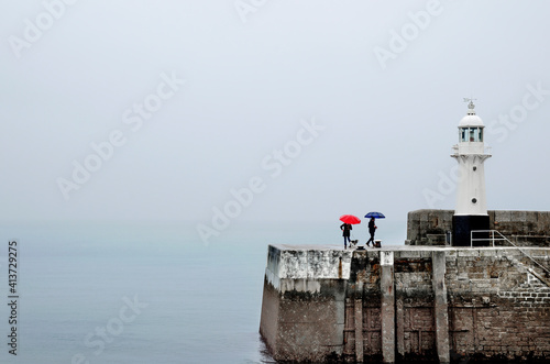 Para spacerująca pod parasolkami z psem nad morzem po nabrzeżu z latarnią 