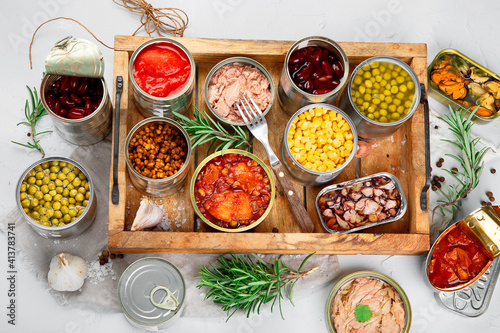 Various canned vegetables, fish and peas in aluminum cans on light gray background.