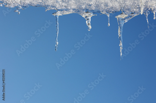 Topniejące sople lodowe na zadaszeniu budynku zimą. 