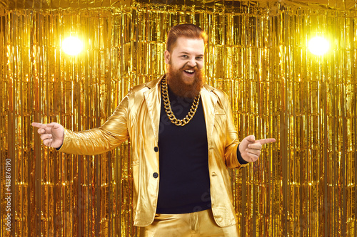 Funny uninhibited plus size young man with ginger beard and mustache in golden suit with bling gold neck chain performing on stage at disco party in night club, dancing, singing songs and having fun