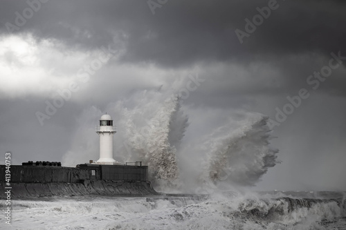 Wintry and stormy seas crashing over breakwater with lighthouse