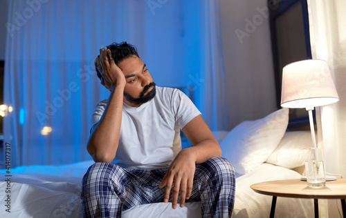 sleeping problem, bedtime and insomnia concept - stressed indian man sitting on bed at night at home