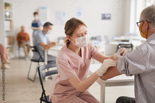 Portrait of young female doctor vaccinating senior man in vaccination center or medical clinic, copy space