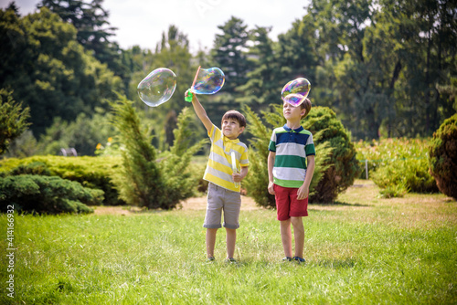 Boy blowing soap bubbles while an excited kid enjoys the bubbles. Happy teenage boy and his brother in a park enjoying making soap bubbles. Happy childhood friendship concept