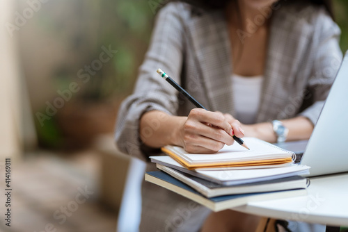 Close up of young woman hand taking notes with laptop at the table office.