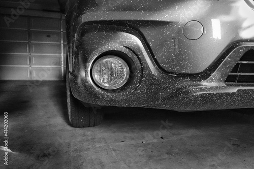 Black and white image of a front bumper of a car covered in dirt while being parked in a garage 