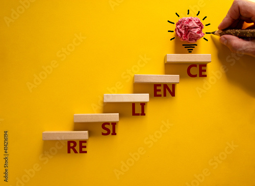 Business and resilience symbol. Wood blocks stacking as step stair, yellow background, copy space. Businessman hand. Word 'resilience'. Conceptual image of motivation. Business and resilience concept.