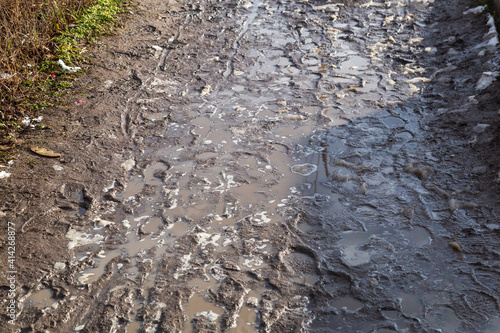 Very dirty pedestrian area with puddles and footprints. Background . The soggy soil of a village road.