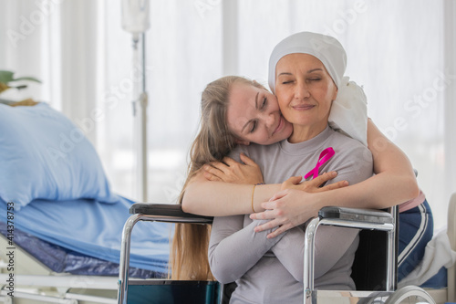 A middle-aged breast cancer woman with clothing around her head effected from chemo therapy sitting on wheel chair and hold hand of her daughter with hope and trust in love.