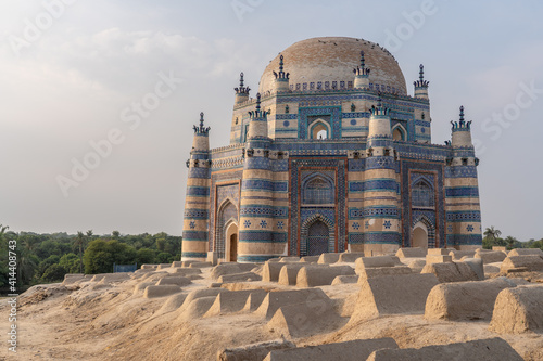 Landscape sunset view of beautiful ancient medieval blue tomb of Bibi Jawindi with traditional graveyard in foreground in Uch Sharif, Bahawalpur, Punjab, Pakistan