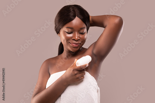 Portrait of smiling black woman applying roller deodorant to armpit zone