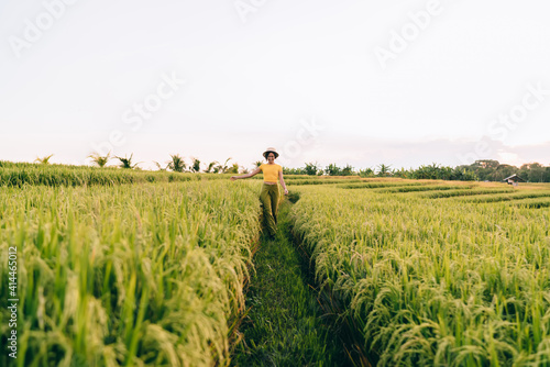 Young cheerful female walking on path among rice fields