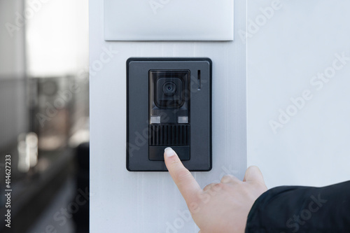 The female hand presses a button doorbell with camera and intercom