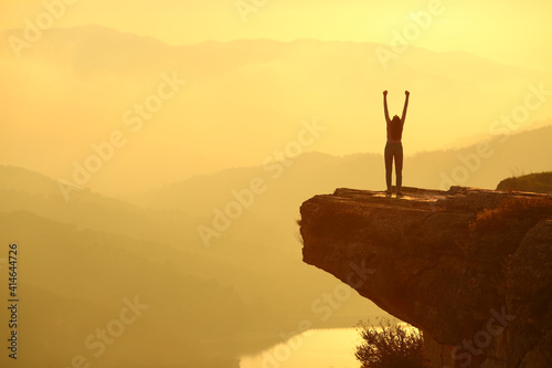 Woman silhouette celebrating in the top of a cliff