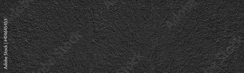 Black old rough concrete wall wide texture. Textured cement plaster surface panorama. Dark grunge background