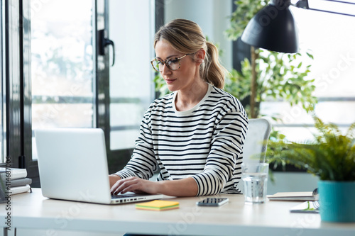 Beautiful mature business woman working while typing with a laptop on a desk in the office at home.