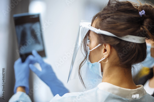 Young doctor shows an X-ray photograph of lungs to the patient and explains the diagnosis. Coronavirus prevention and prophylaxy. Hospital and medicine concept.