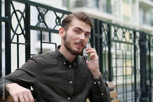 Young handsome businessman sits on bench and talks on mobile phone