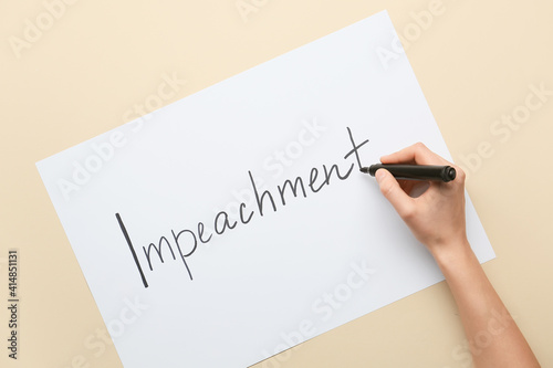 Hand writing text IMPEACHMENT on paper against color background