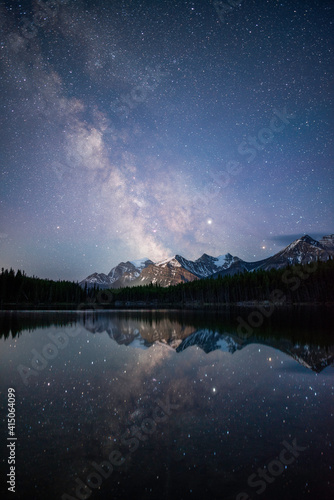 The Milky Way reflecting off of the calm waters of Herbert Lake while the town of Lake Louise illuminated the Canadian Rockies.