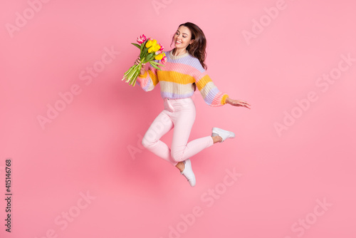 Full length body size view of pretty trendy cheerful girl jumping holding tulips good mood isolated over pink pastel color background