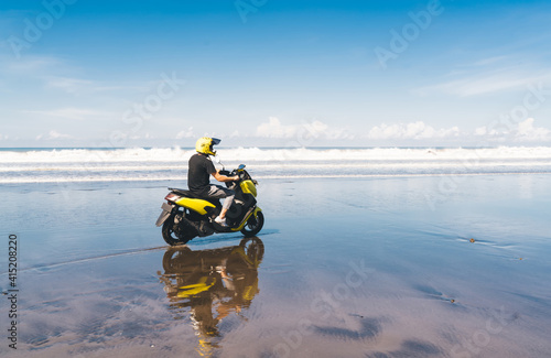 Unrecognizable man in helmet riding motorbike on sandy sea coastline