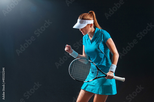 Tennis player with racket in blue costume. Woman athlete playing on black background.