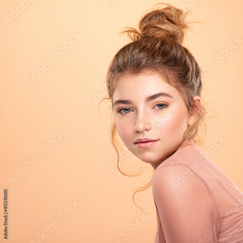 Closeup portrait of an young girl over colored background. Photo of a fashion model posing at studio. Pretty young woman with brown hair looking at camera. Beauty portrait.