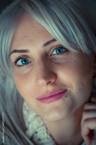 close up indoor portrait of an attractive young woman with blue eyes and platinum-blond hair, on a grey background