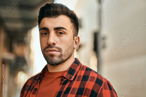 Young hispanic man with serious expression standing at the city.