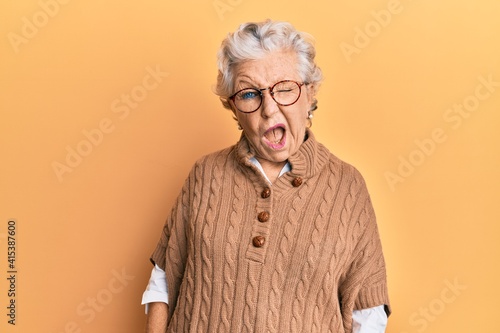 Senior grey-haired woman wearing casual clothes and glasses winking looking at the camera with sexy expression, cheerful and happy face.