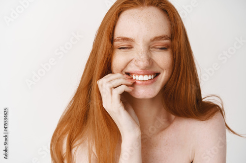 Close-up of happy redhead woman with pale no makeup skin and perfect smile, laughing and looking joyful, standing naked over white background