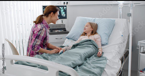 Young mother interacting and holding hand of daughter in ward at hospital