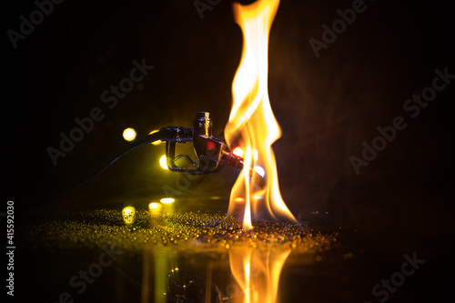 Creative concept. Silhouette of gasoline pistol miniature on dark toned foggy background. Close up. Industrial decorated elements on background.