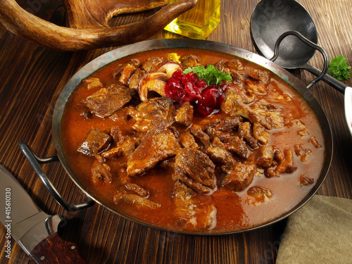 Wild Game Meat Goulash in a Pan with Cranberries on wooden Background