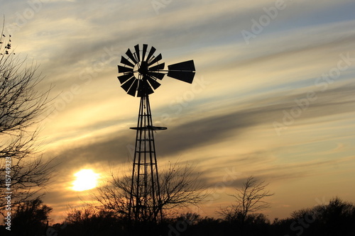 Kansas colorful Sunset with a Windmill and tree silhouette with clouds and the sun north of Hutchinson Kansas USA.