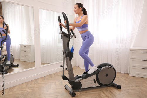 Woman using modern elliptical machine at home