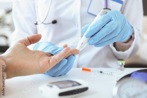 Doctor with gloves piercing patients finger with lancet closeup