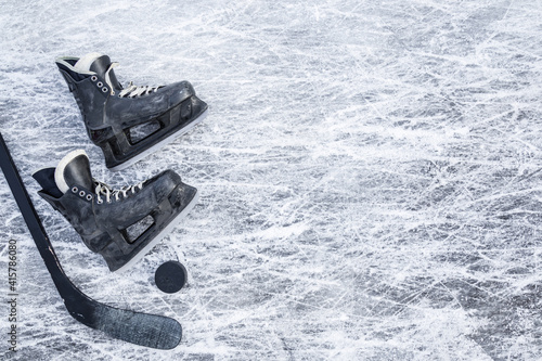 Old scratched black hockey male skates, stick and rubber puck on ice background. Closeup. Empty place for text. Top down view.