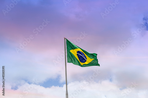 Bandeira do Brasil hasteada, balançando ao vento com o céu e nuvens ao fundo.