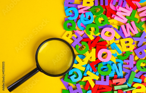 Magnifying glass with colorful alphabet on yellow background, Copy space.Education concept.