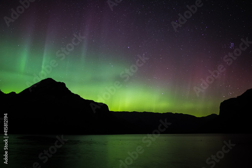 Red, Green and yellow Aurora Borealis (Northern Lights) from a lake in the Canadian Rockies during a spring night, Lake Minnewanka, Banff National Park, Alberta, Canada