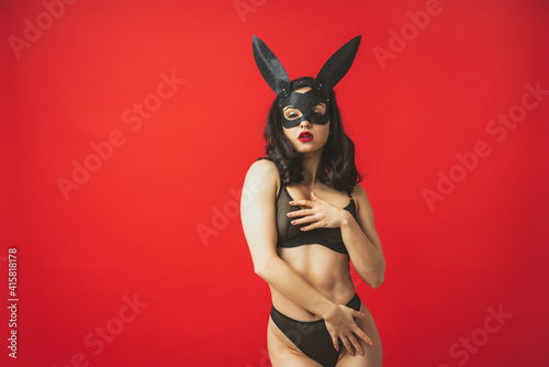 Image of a woman wearing a sexy rabbit mask and posing on a red colored background