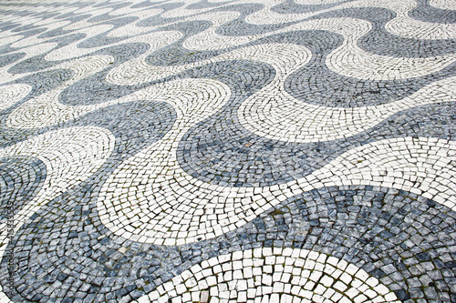 Photo of paving stones in perspective. The drawing is lined with cobblestones in the form of white and gray waves. Traditional street paving in Lisbon and Rio de Janeiro.