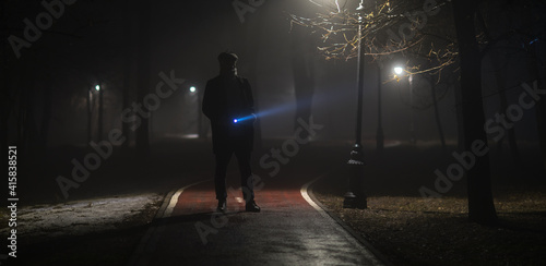 detective with a flashlight in the forest at night in the fog